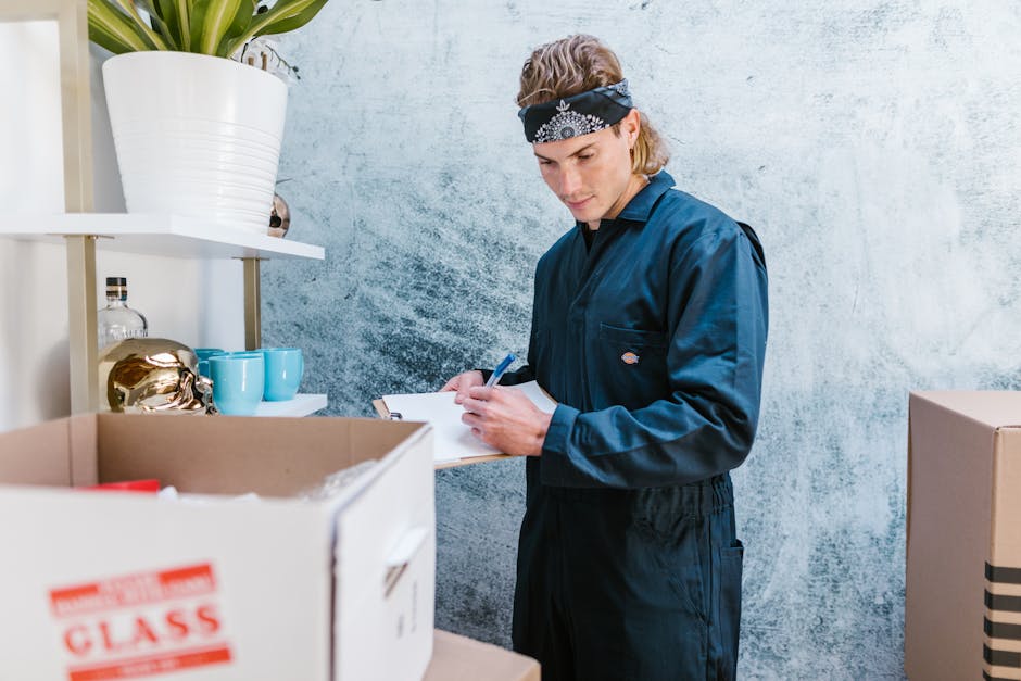A professional mover from Londonmanandavan.org.uk is carefully carrying a green velvet upholstered sofa, which is partially wrapped in protective packaging, through an interior doorway during a home r