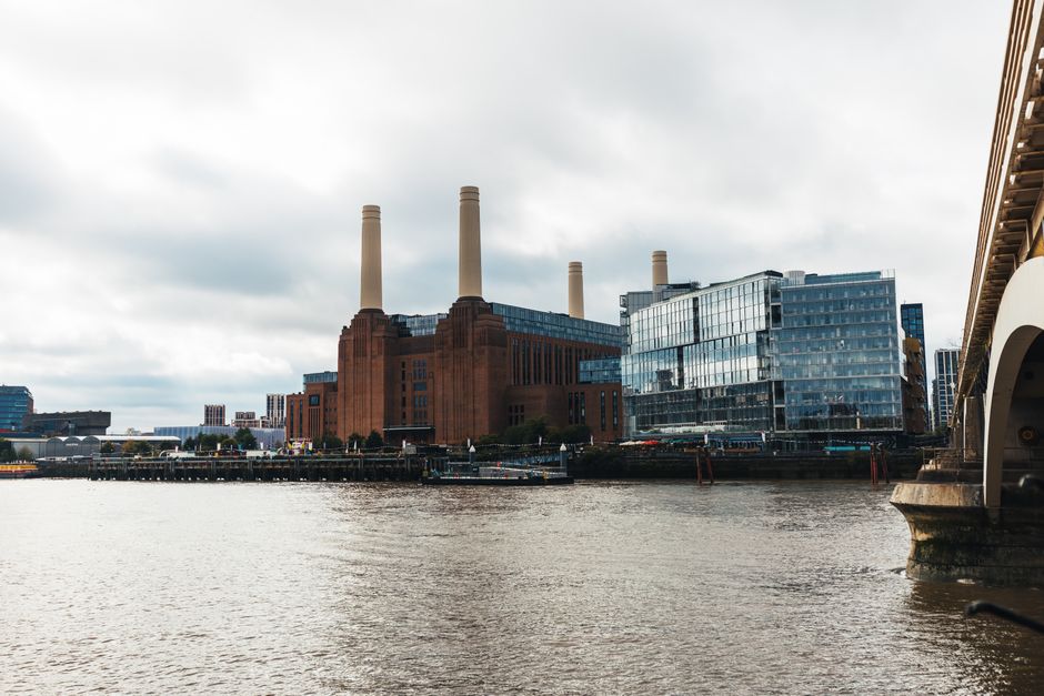 Photograph taken during daylight showing the chimney stacks of a traditional industrial building, with two large off-white cylindrical chimneys positioned on a brick structure. The chimneys are vertic