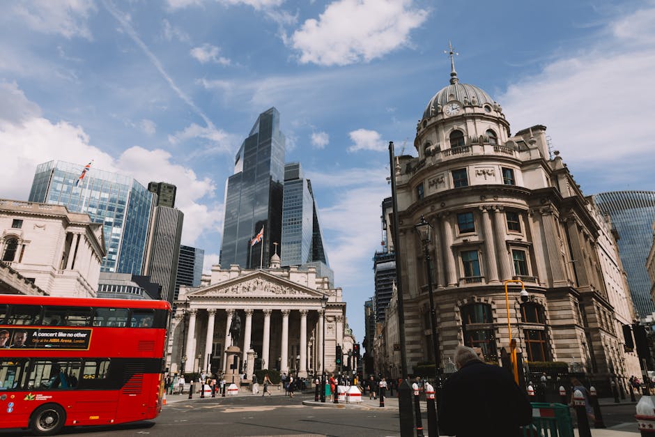 A city street in London during daytime features a mix of historic and modern architecture, including a prominent domed building with classical columns and detailed stonework, surrounded by tall glass 