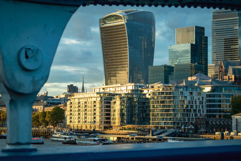A city street in London during daytime features a mix of historic and modern architecture, including a prominent domed building with classical columns and detailed stonework, surrounded by tall glass 